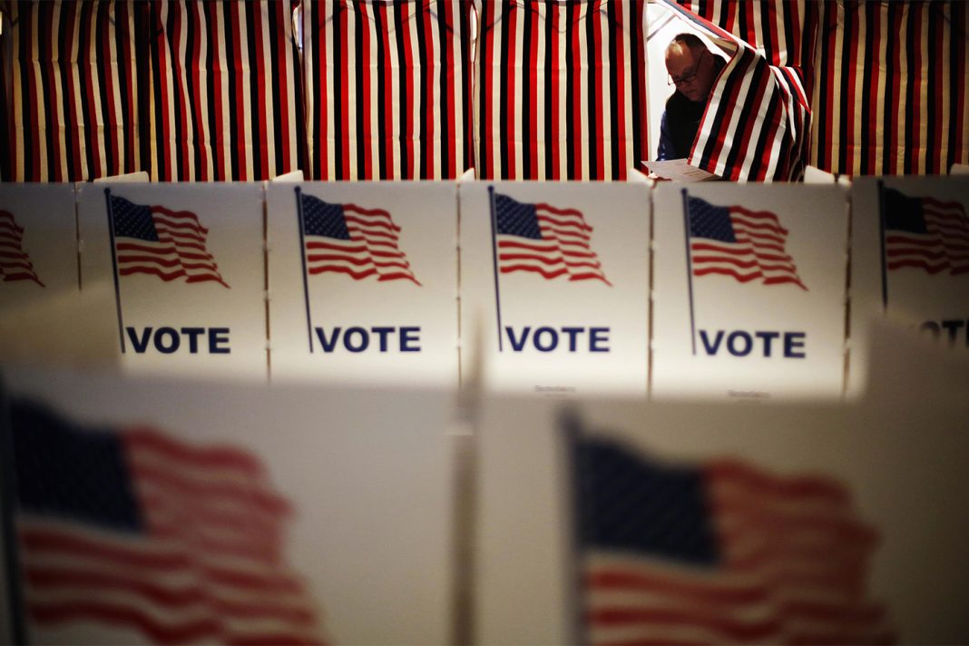 Polling booths are covered with prints of the American flag featuring the word 'VOTE' in blue.